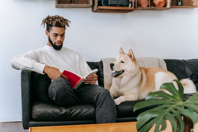 a-man-sitting-on-a-couch-reading-a-book-while-a-large-dog-rests-beside-him