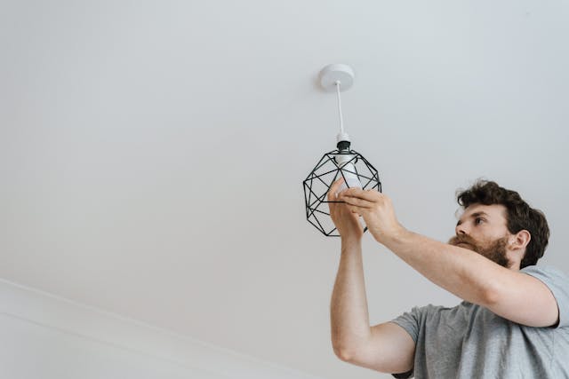 a-person-installing-a-light-bulb-into-a-geometric-pendant-light-fixture-on-the-ceiling