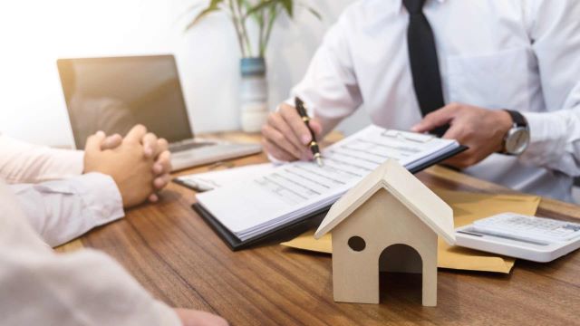 a-person-reviewing-paperwork-with-a-small-wooden-house-model-on-the-desk