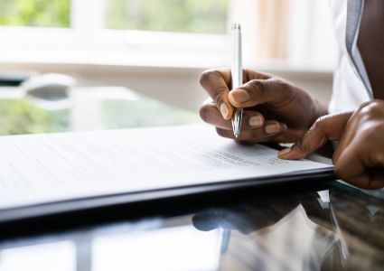 a-person-signing-a-document-with-a-pen-on-a-reflective-desk-surface