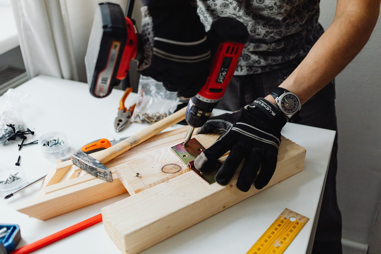 a-person-using-a-power-drill-on-a-wooden-plank-with-tools-and-screws-on-a-table