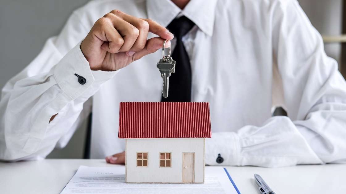 person holding keys over a house figurine