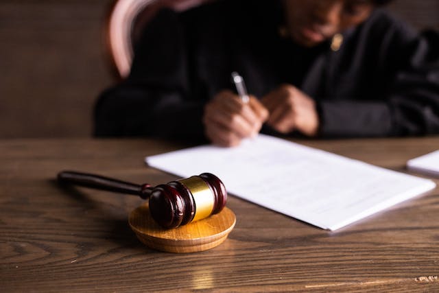 person-sitting-at-table-writing-on-paper-with-a-gavel-in-front-of-it