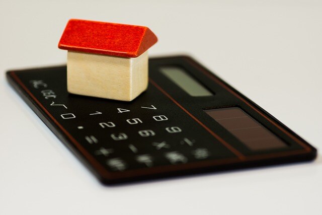 small toy house made of wood with a red roof sits on a black calculator on a white background